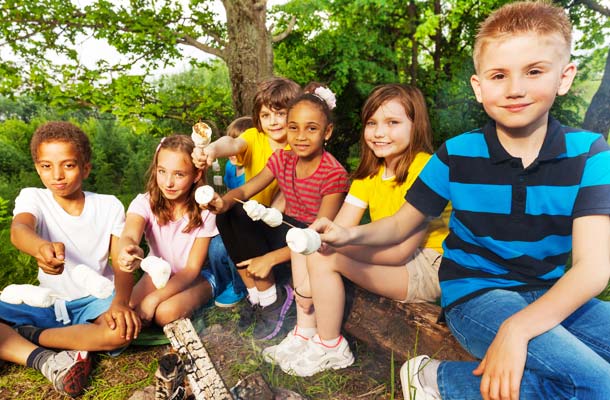 Group of kids sitting near bonfire with marshmallow smores during camping in the forest together